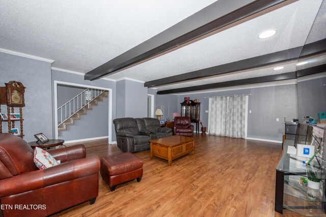 living area featuring beamed ceiling, wood finished floors, crown molding, baseboards, and stairs