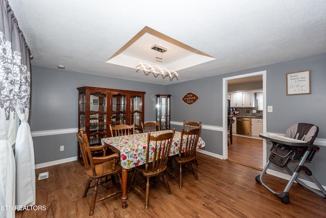 dining room with visible vents, a wainscoted wall, a tray ceiling, wood finished floors, and a textured ceiling