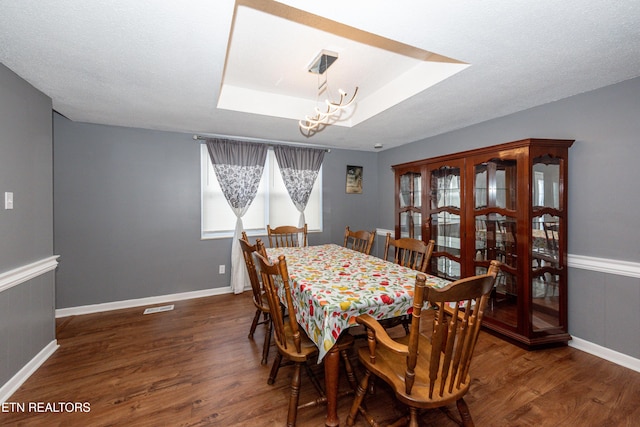 dining room featuring a tray ceiling, a notable chandelier, visible vents, and wood finished floors