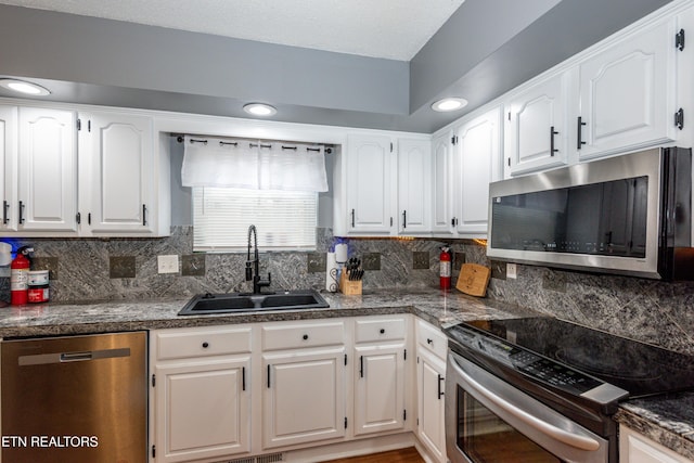 kitchen featuring a sink, backsplash, dark countertops, white cabinetry, and stainless steel appliances