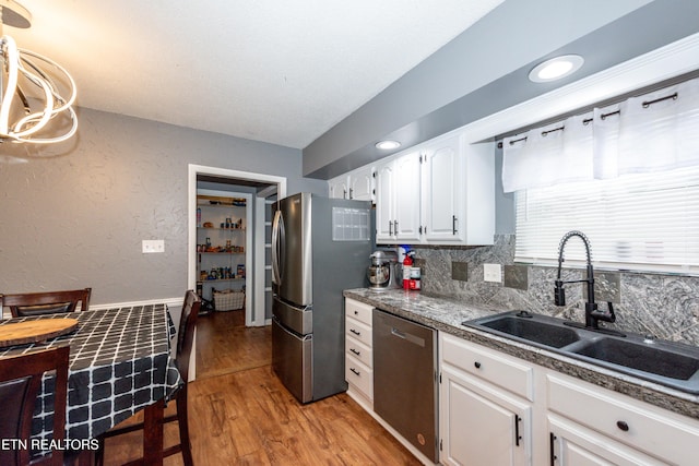 kitchen with light wood finished floors, a sink, appliances with stainless steel finishes, white cabinetry, and tasteful backsplash
