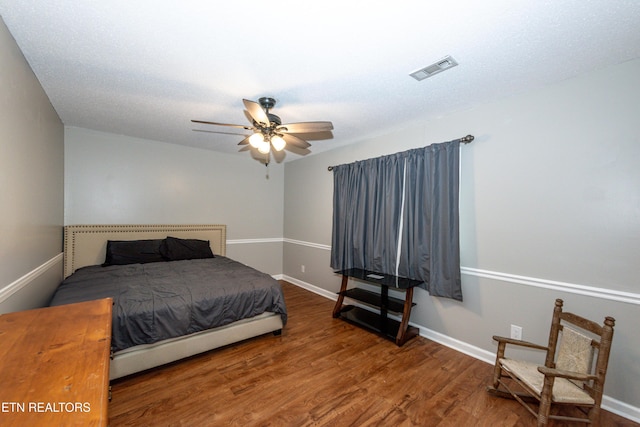 bedroom with a ceiling fan, wood finished floors, visible vents, and baseboards