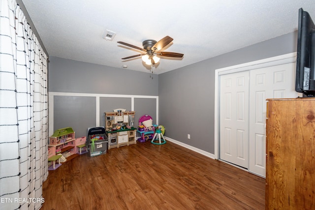 recreation room featuring visible vents, a textured ceiling, wood finished floors, baseboards, and ceiling fan