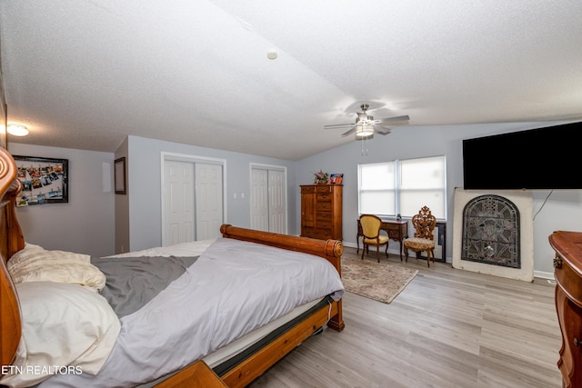 bedroom featuring two closets, ceiling fan, vaulted ceiling, wood finished floors, and a textured ceiling