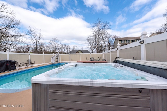 view of swimming pool featuring a water slide, a fenced backyard, and a hot tub