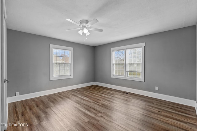 spare room with ceiling fan, visible vents, baseboards, and wood finished floors