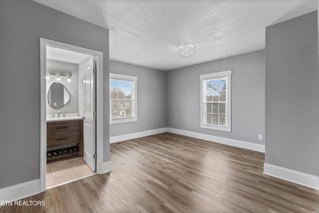 unfurnished bedroom with a sink, a textured ceiling, baseboards, and wood finished floors