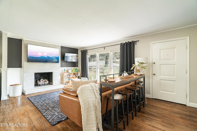 living room featuring a brick fireplace, crown molding, baseboards, and wood finished floors