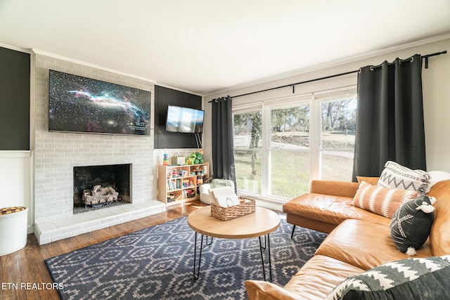 living area with a wainscoted wall, wood finished floors, a fireplace, and crown molding