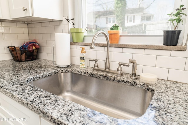 room details featuring decorative backsplash, white cabinets, light stone countertops, and a sink