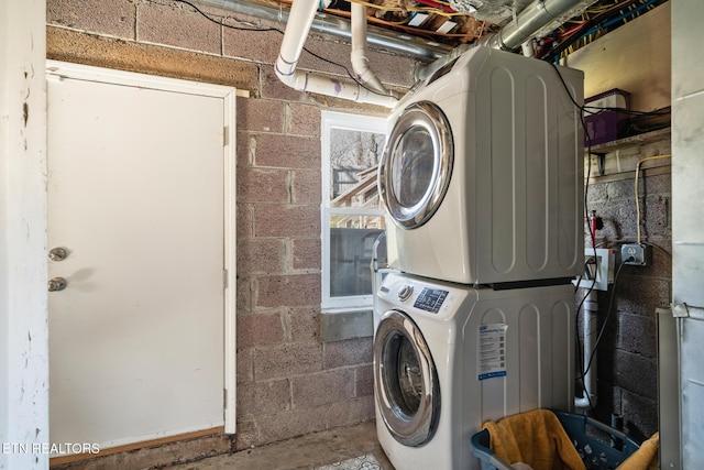 washroom featuring concrete block wall, laundry area, and stacked washing maching and dryer