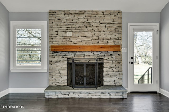 room details featuring a stone fireplace, wood finished floors, and baseboards