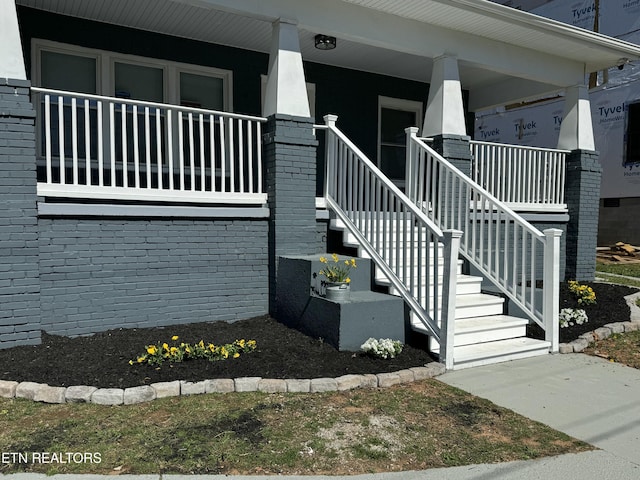 doorway to property featuring brick siding and a porch