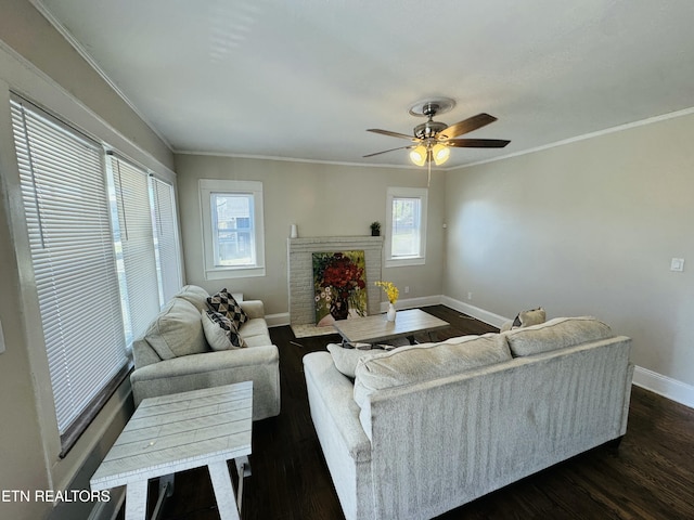 living area featuring baseboards, dark wood finished floors, ceiling fan, ornamental molding, and a brick fireplace