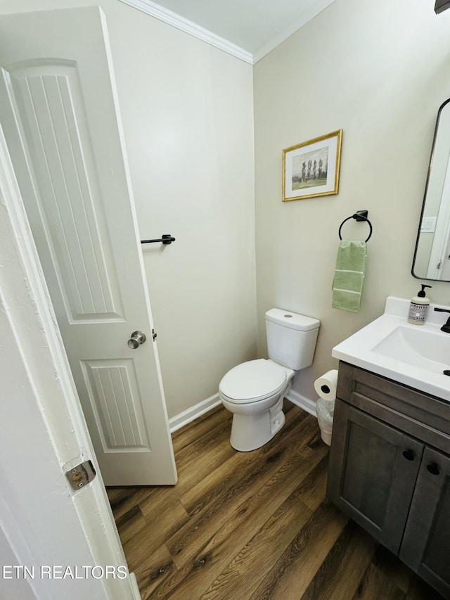 half bathroom featuring toilet, ornamental molding, wood finished floors, baseboards, and vanity