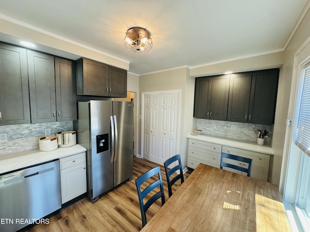 kitchen featuring tasteful backsplash, light countertops, ornamental molding, appliances with stainless steel finishes, and light wood-style floors