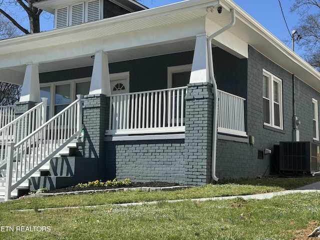 view of side of property featuring stairway, brick siding, covered porch, and central AC
