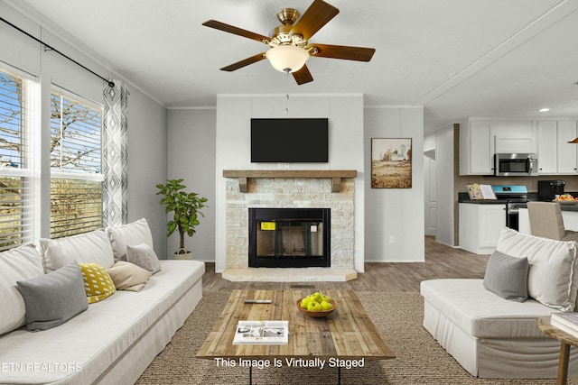 living area featuring baseboards, a stone fireplace, a ceiling fan, crown molding, and light wood-style floors