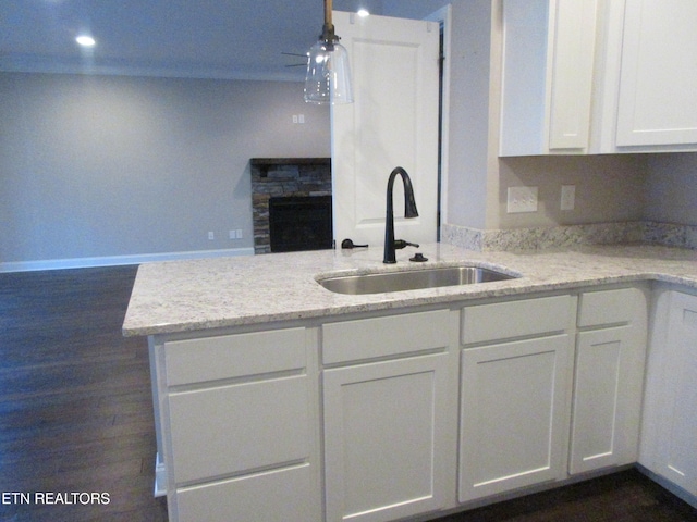 kitchen featuring light stone counters, a sink, white cabinetry, and a stone fireplace