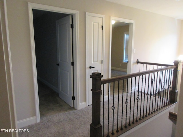 hallway featuring carpet flooring, an upstairs landing, and baseboards