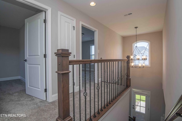 hallway featuring baseboards, a chandelier, an upstairs landing, visible vents, and carpet