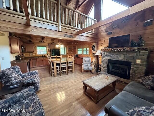 living room featuring wooden walls, beam ceiling, a fireplace, light wood-type flooring, and a towering ceiling