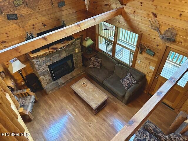 living room with a stone fireplace, wood finished floors, and wooden walls