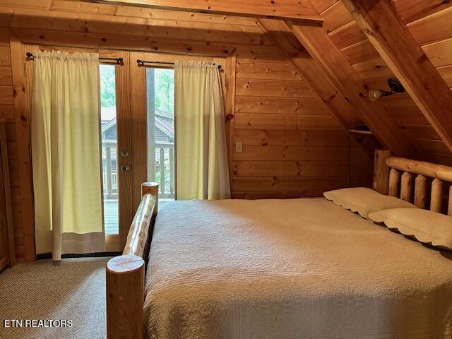 bedroom featuring wooden walls, carpet floors, access to outside, and lofted ceiling