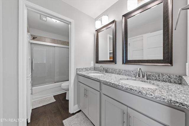 bathroom with double vanity, wood finished floors, bath / shower combo with glass door, and a sink