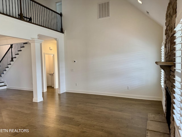 unfurnished living room with visible vents, stairway, decorative columns, dark wood finished floors, and a high ceiling