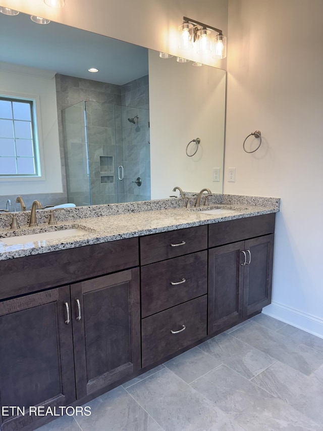 full bathroom with baseboards, double vanity, a sink, and a stall shower