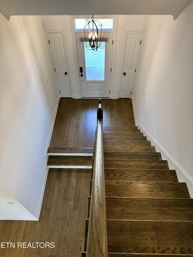 staircase featuring hardwood / wood-style floors, a notable chandelier, and baseboards