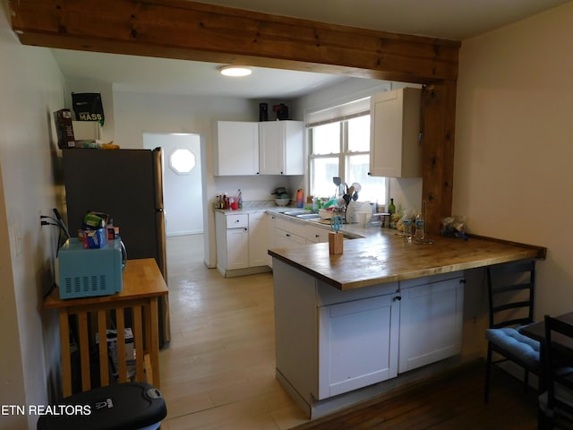 kitchen with beam ceiling, freestanding refrigerator, white cabinetry, light wood-style floors, and a peninsula