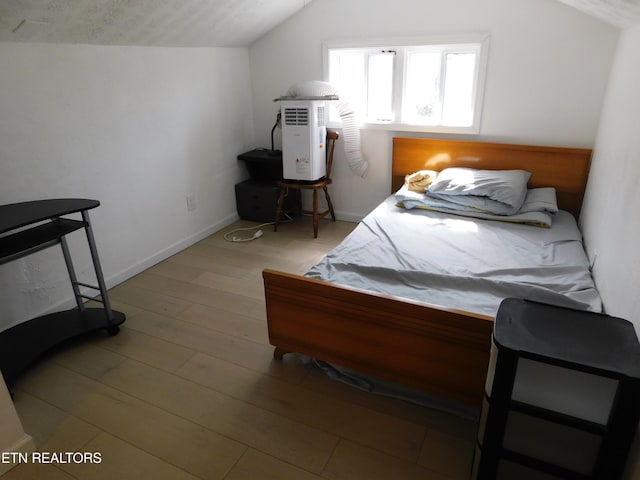 bedroom with baseboards, light wood-style floors, and vaulted ceiling