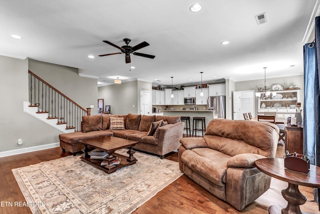living room with dark wood-style floors, ceiling fan with notable chandelier, and ornamental molding