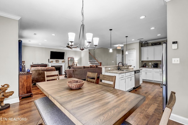 dining space featuring ornamental molding, a ceiling fan, dark wood-style floors, a fireplace, and stairs