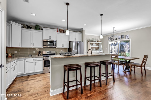 kitchen featuring backsplash, stainless steel appliances, a notable chandelier, and wood finished floors