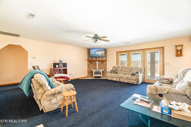 carpeted living room with a ceiling fan, visible vents, a wood stove, french doors, and a textured ceiling