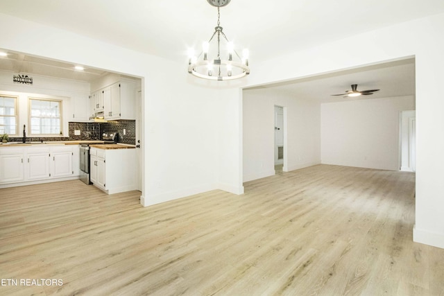 interior space featuring baseboards, a sink, ceiling fan with notable chandelier, and light wood-type flooring