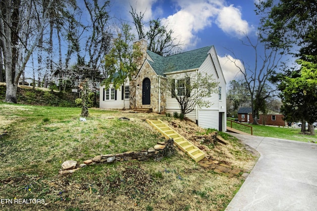 view of front of house featuring stone siding, a garage, a front yard, a chimney, and concrete driveway