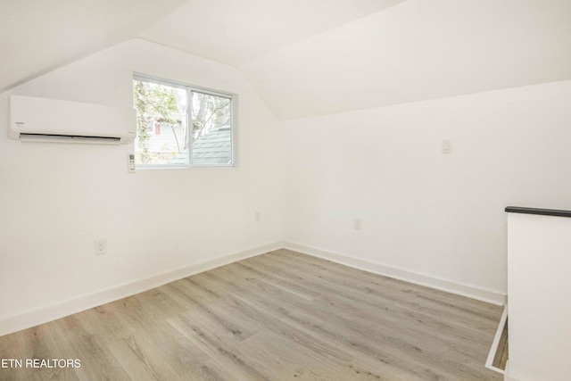 bonus room with light wood-style floors, baseboards, a wall unit AC, and lofted ceiling