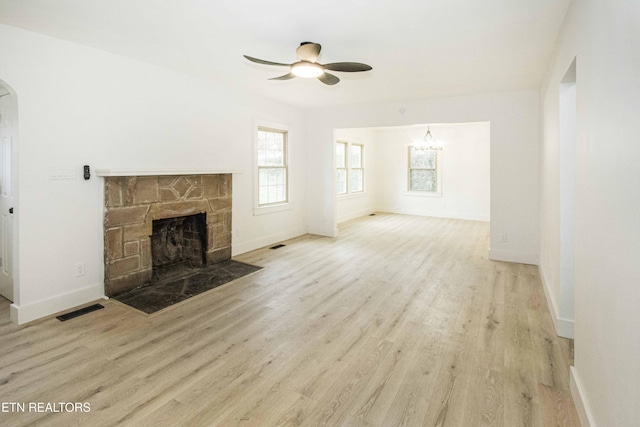 unfurnished living room featuring visible vents, wood finished floors, a fireplace, baseboards, and ceiling fan with notable chandelier