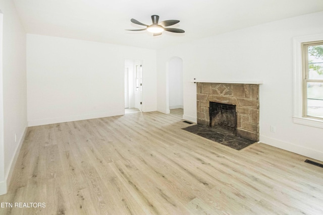 unfurnished living room with visible vents, a ceiling fan, wood finished floors, a stone fireplace, and arched walkways