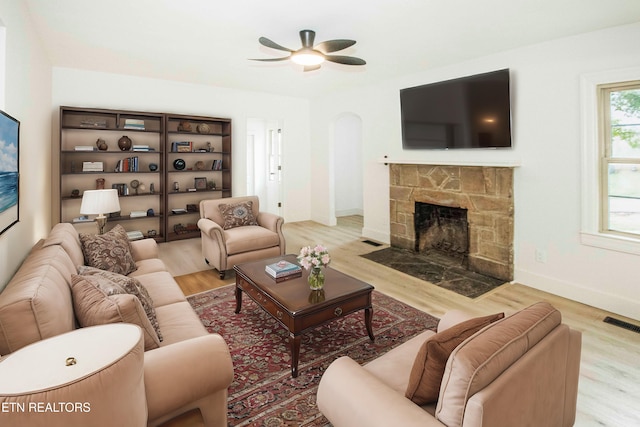 living area featuring ceiling fan, a stone fireplace, visible vents, arched walkways, and wood finished floors