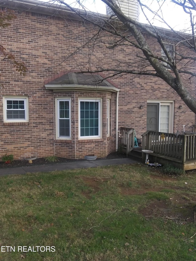 view of side of home featuring a yard, brick siding, and a deck