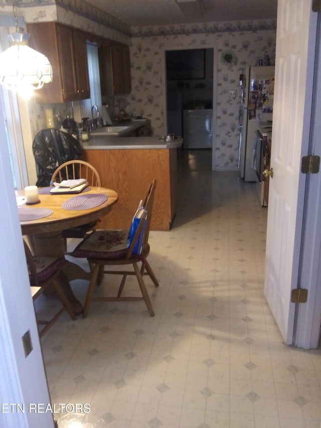 kitchen featuring washer / dryer, a sink, wallpapered walls, and light floors