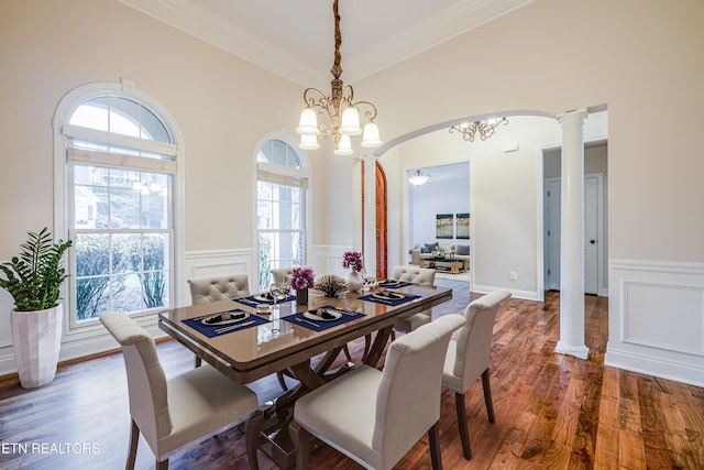dining room featuring wood finished floors, crown molding, arched walkways, a notable chandelier, and wainscoting