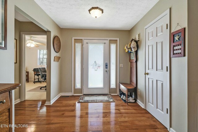 foyer entrance with baseboards, a textured ceiling, and wood finished floors
