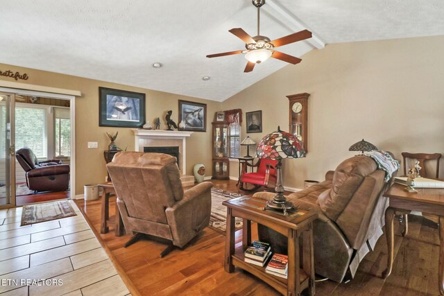 living room featuring wood finished floors, baseboards, lofted ceiling with beams, a fireplace, and ceiling fan