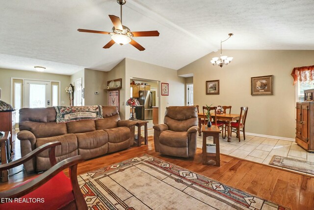 living area with light wood-type flooring, a textured ceiling, vaulted ceiling, and ceiling fan with notable chandelier